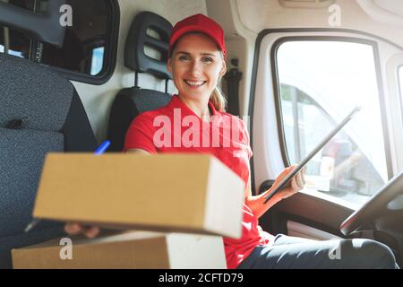 jeune femme heureuse employée de service de livraison assis dans une camionnette et livraison d'une boîte Banque D'Images