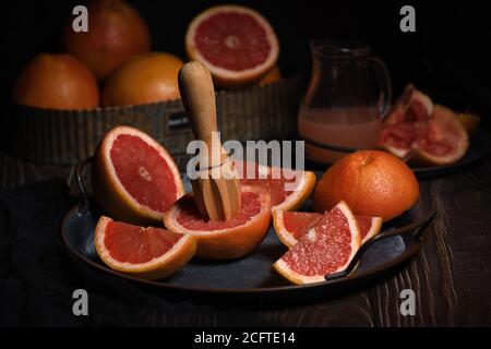 Tranches de pamplemousse frais préparées pour faire du jus frais pressé sur un plateau, fond sombre Banque D'Images