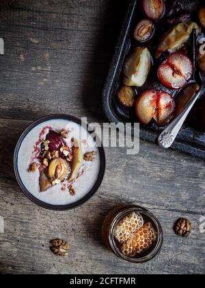 Prunes grillées, greentons rouges et pommes sur une plaque à pâtisserie. Porridge de sarrasin avec fruits et noix dans un bol. Miel sur table en bois. Vue de dessus. Banque D'Images