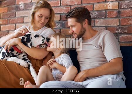 portrait de la jeune famille caucasienne s'amuser avec le chien à la maison, les parents et l'enfant se reposer, se détendre à la maison, prendre soin du chien dalmatien Banque D'Images