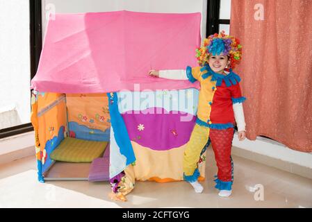 Drôle petite fille en costume de perruque multicolore de clown regardant l'appareil photo. Banque D'Images