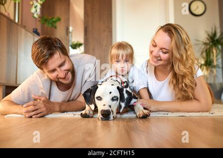 portrait de la jeune famille caucasienne s'amuser avec le chien à la maison, les parents et l'enfant se reposer, se détendre à la maison, prendre soin du chien dalmatien Banque D'Images