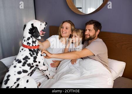 portrait de la jeune famille caucasienne s'amuser avec le chien à la maison, les parents et l'enfant se reposer, se détendre à la maison, prendre soin du chien dalmatien Banque D'Images