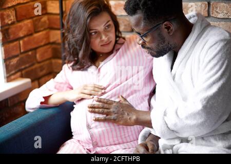 beau couple marié attendez bébé, ils s'assoient avec un ordinateur portable à la maison, parler. africain se sentent heureux, coup ventre Banque D'Images