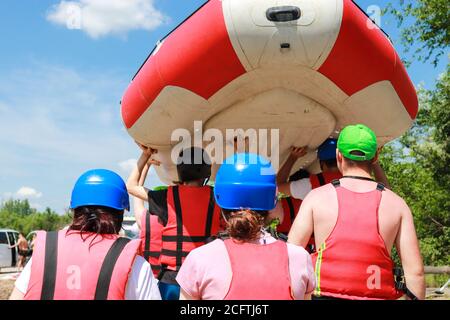 Équipe de rafting en équipement sportif après un rafting réussi le long la rivière porte un bateau gonflable en caoutchouc au-dessus de la placez l'alliage à l'endroit où il commence Banque D'Images