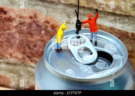 Image conceptuelle de la figure miniature des ouvriers qui fixent un crochet de grue à l'anneau tirer d'une boîte de boissons gazeuses en aluminium Banque D'Images