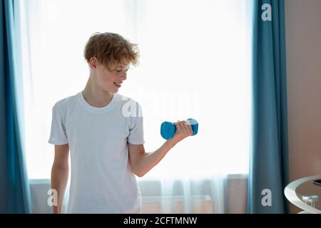 beau garçon heureux ado faire le sport traning à la maison seul. utilisez des haltères Banque D'Images