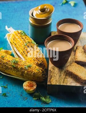 Vue de dessus du thé au lait chaud préparé avec du maïs grillé et du pain grillé frais. Délicieux Cornouailles grillées et deux tasses de Masala Chai, un LUN indien idéal Banque D'Images