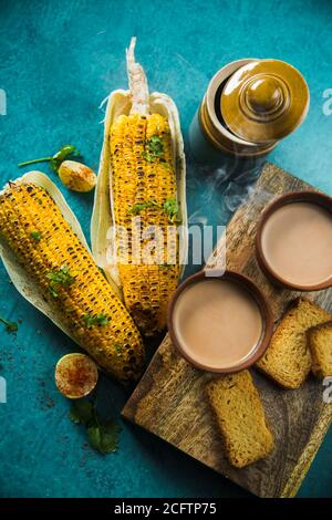 Vue de dessus du thé au lait chaud préparé avec du maïs grillé et du pain grillé frais. Délicieux Cornouailles grillées et deux tasses de Masala Chai, un LUN indien idéal Banque D'Images