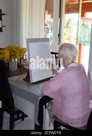 Kiev, Ukraine, septembre 2020. Une femme âgée tient un pinceau et peint une image sur toile par nombres. Passe-temps créatif. Activités de loisirs à la maison Banque D'Images