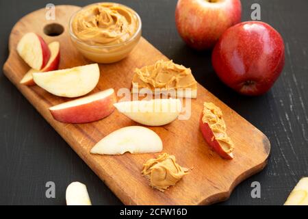 Pommes rouges crues et beurre de cacahuète sur une planche de bois rustique sur une surface noire, vue à angle bas. Gros plan. Banque D'Images