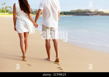 Lune de miel pieds nus couple tenant les mains marchant sur la plage romantique vacances laissant des empreintes dans le sable doré avec les pieds. Jeunes de Banque D'Images