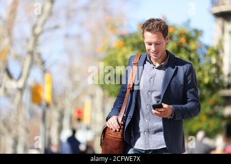 Jeune homme d'affaires urbain professionnel sur smartphone marchant dans la rue en utilisant application pour téléphone mobile envoyant des sms sur un smartphone avec smart décontracté Banque D'Images