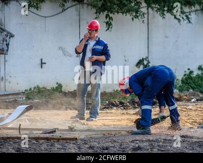 Moscou. Russie. 06 septembre 2020 des ouvriers en uniforme bleu et en casque de sécurité rouge sur un chantier de construction coupent du métal à l'aide d'une meuleuse. Étincelles de Banque D'Images