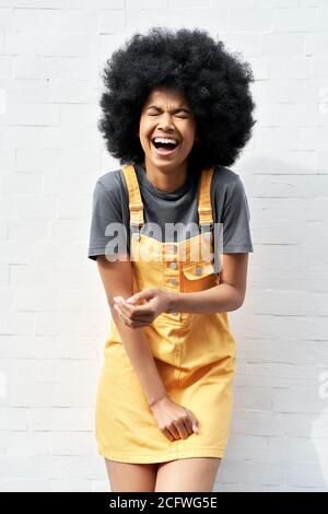 Drôle de dame africaine avec les cheveux afro riant debout contre le mur de brique blanche. Banque D'Images