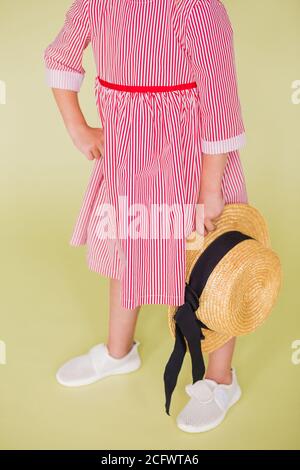 Une fille de baskets rouges et blanches tient un chapeau de paille dans ses mains. Fille debout sur un fond vert Banque D'Images