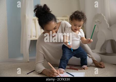 Une jeune maman afro-américaine souriante et bienveillante enseignant le dessin de bébé. Banque D'Images