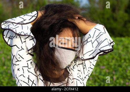 Femme élégante portant un masque de protection et posant sur un fond vert naturel à l'extérieur. Banque D'Images