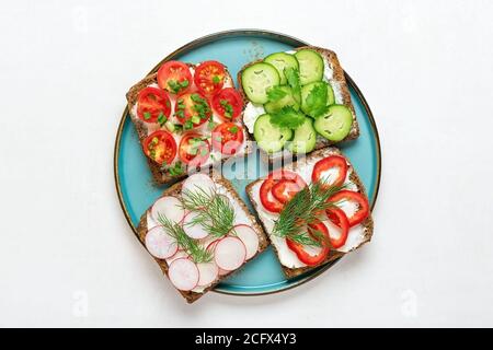 Variété de sandwiches pour le petit déjeuner - tranche de pain noir de grain entier, poivre, fromage à la crème, concombres, radis, tomates cerises, garni d'aneth Banque D'Images