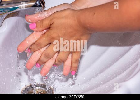 Gros plan d'une femme se lavant les mains à l'eau du robinet. Ongles roses. Concept d'hygiène. Banque D'Images