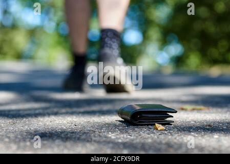 Photo du trottoir et des jambes d'un homme qui perdu un portefeuille en cuir noir en marchant Banque D'Images