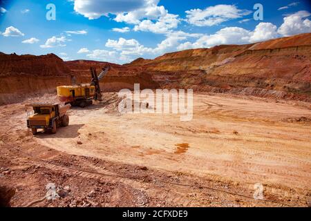 Exploitation et transport du minerai d'aluminium. Carrière d'argile de bauxite (mine). Pelle hydraulique chargeant le minerai sur le camion-benne Belaz. Ciel bleu avec nuages clairs. Banque D'Images