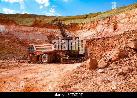 Exploitation et transport du minerai d'aluminium. La pelle hydraulique charge de l'argile à bauxite sur le tombereau de carrière Hitachi. Banque D'Images