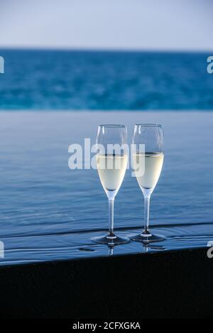 Une paire de flûtes à champagne sont situées au bord d'une piscine à débordement pour un couple à profiter sur leur terrasse privée dans un complexe de luxe aux Maldives. Banque D'Images