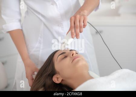 Femme aux cheveux foncés ayant des procédures de visage au laser en clinique Banque D'Images