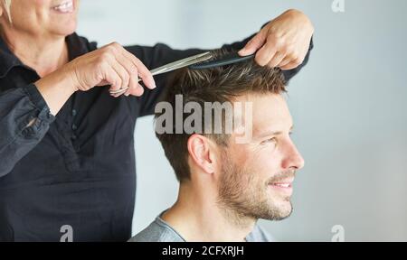 Femme coupant les cheveux d'un homme avec des ciseaux au coiffeur Banque D'Images