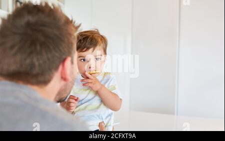 Le père regarde son enfant manger des biscuits dans la cuisine Banque D'Images