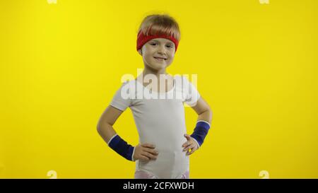 Petite mignonne caucasienne fille en blanc sportswear faire fitness gymnastique à la maison exercices. Entraînement pour les enfants. Jeune enfant sportif en costume de sport pour se réchauffer et s'étirer. Isolé seul sur fond jaune Banque D'Images