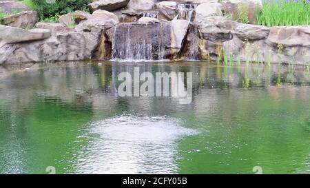 Une petite cascade décorative s'éclabousse dans l'étang. Aménagement paysager en pierre et en eau dans un parc ou un jardin. Paysage naturel dans la forêt tropicale. Banque D'Images