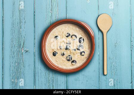 au-dessus de la vue de flocons d'avoine sains ou de porridge avec myrtilles dedans bol rustique table en bois bleu Banque D'Images