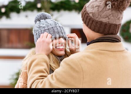 Couple romantique ayant du plaisir à l'extérieur en hiver, homme jouant avec le chapeau de petite amie Banque D'Images