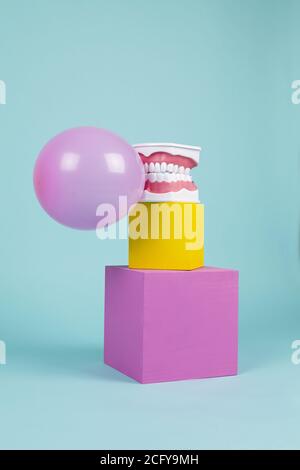 un modèle anatomique de dent en plastique pour apprendre à brosser les dents en tenant une boule de gomme à mâcher sur des cubes colorés. Humour et ambiance pop. Minimale Banque D'Images
