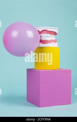 un modèle anatomique de dent en plastique pour apprendre à brosser les dents en tenant une boule de gomme à mâcher sur des cubes colorés. Humour et ambiance pop. Minimale Banque D'Images