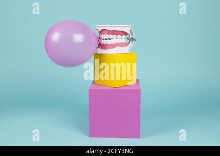 un modèle anatomique de dent en plastique pour apprendre à brosser les dents en tenant une boule de gomme à mâcher sur des cubes colorés. Humour et ambiance pop. Minimale Banque D'Images