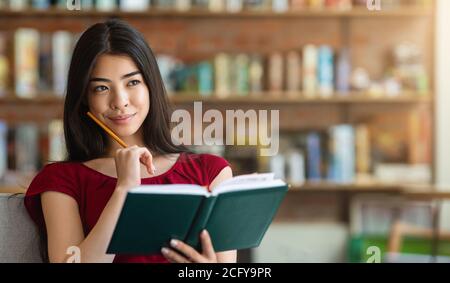 Réflexion sur les plans futurs. Pensive Asian Girl assis avec le Bloc-notes au café Banque D'Images