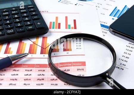 Vue d'un espace de travail de bureau avec des tableaux financiers et des numéros, avec calculatrice, loupe et téléphone portable. Stylo bleu sur livres blancs. Banque D'Images