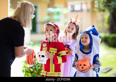 Les enfants se déguent en costume d'Halloween. Les enfants de couleur s'habillent avec un seau à bonbons dans la rue de banlieue. Petit garçon et fille trick ou traiter le wi Banque D'Images