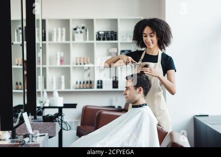 Femme noir coiffeur coupant les cheveux de jeune homme client Banque D'Images