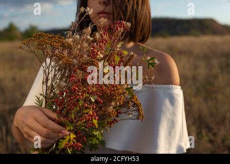 portrait d'une belle fille en gros plan. Il tient un bouquet de fleurs sauvages dans ses mains. Dans une robe blanche. Sur fond de ciel bleu nuageux. Ha Banque D'Images