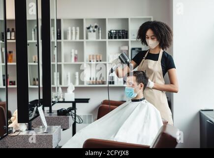 Coiffeur séchage des cheveux de client masculin, tous deux observant les mesures de sécurité Banque D'Images