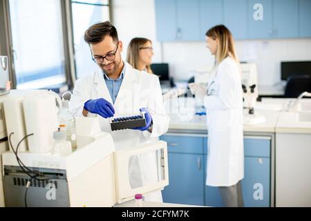 Beau chercheur en vêtements de travail de protection debout dans le laboratoire et analyse d'échantillons liquides Banque D'Images