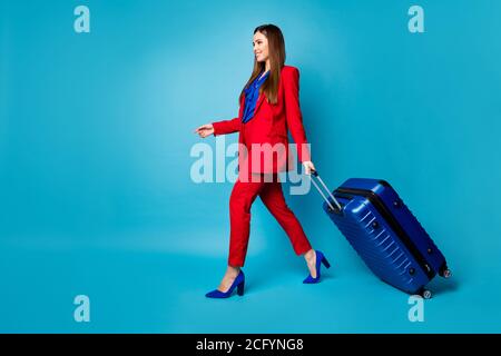 Pleine photo de profil de corps de femme d'affaires attrayante tenir grand valise à roulettes avec inscription pour les voyages d'affaires, porter un luxe rouge costume haut chemisier Banque D'Images