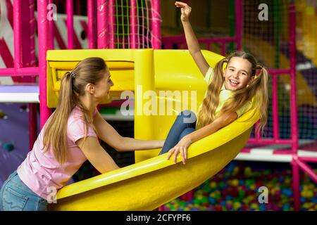 Jeune maman avec sa fille s'amuser sur le toboggan de terrain de jeu au centre intérieur pour enfants Banque D'Images