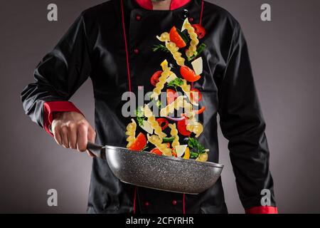 Gros plan du chef qui jette des pâtes italiennes avec des légumes dans l'air. Concept de préparation des aliments Banque D'Images