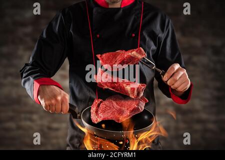 Gros plan du chef qui lance des steaks de bœuf crus dans l'air. Concept de la préparation des aliments, du gril et du barbecue Banque D'Images