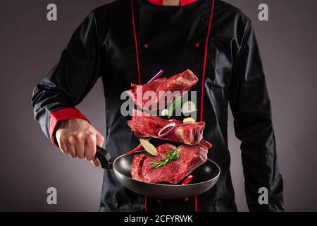 Gros plan du chef qui lance des steaks de bœuf crus dans l'air. Concept de préparation des aliments Banque D'Images